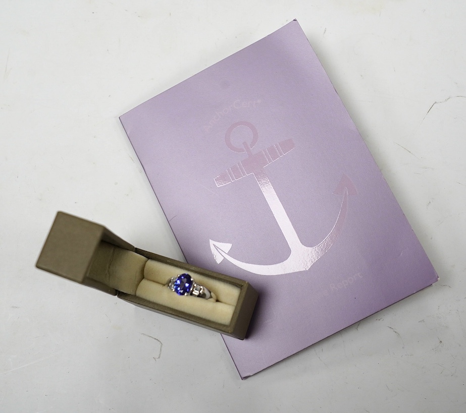 A modern 18ct gold and single stone oval cut tanzanite set ring, with baguette cut diamond cluster set shoulders, with accompanying AnchorCert report, stating the stone to weigh 1.20ct, size L, gross weight 4.1 grams. Co